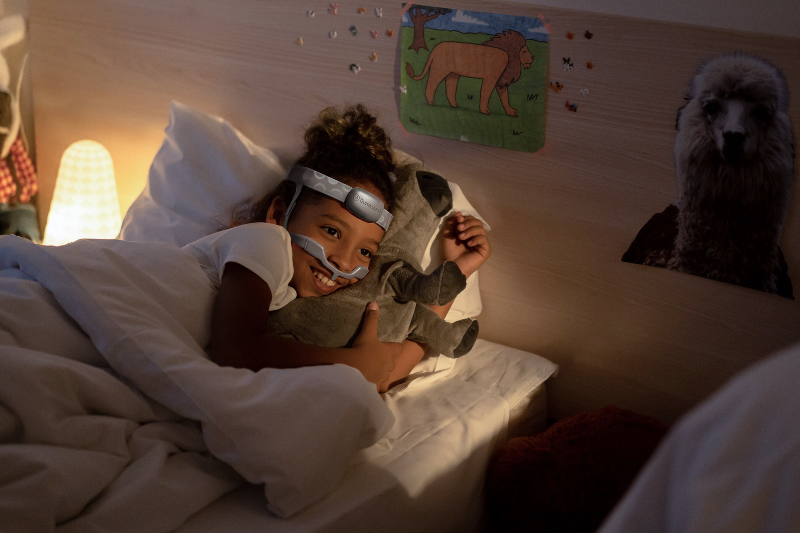 Child lying in bed at night wearing the Dormovision X™ Home PSG system and holding a small toy.